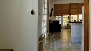 Un pasillo con piso de baldosas, un banco de madera y un acceso a una zona de cocina con salpicadero de azulejos y armarios de madera.