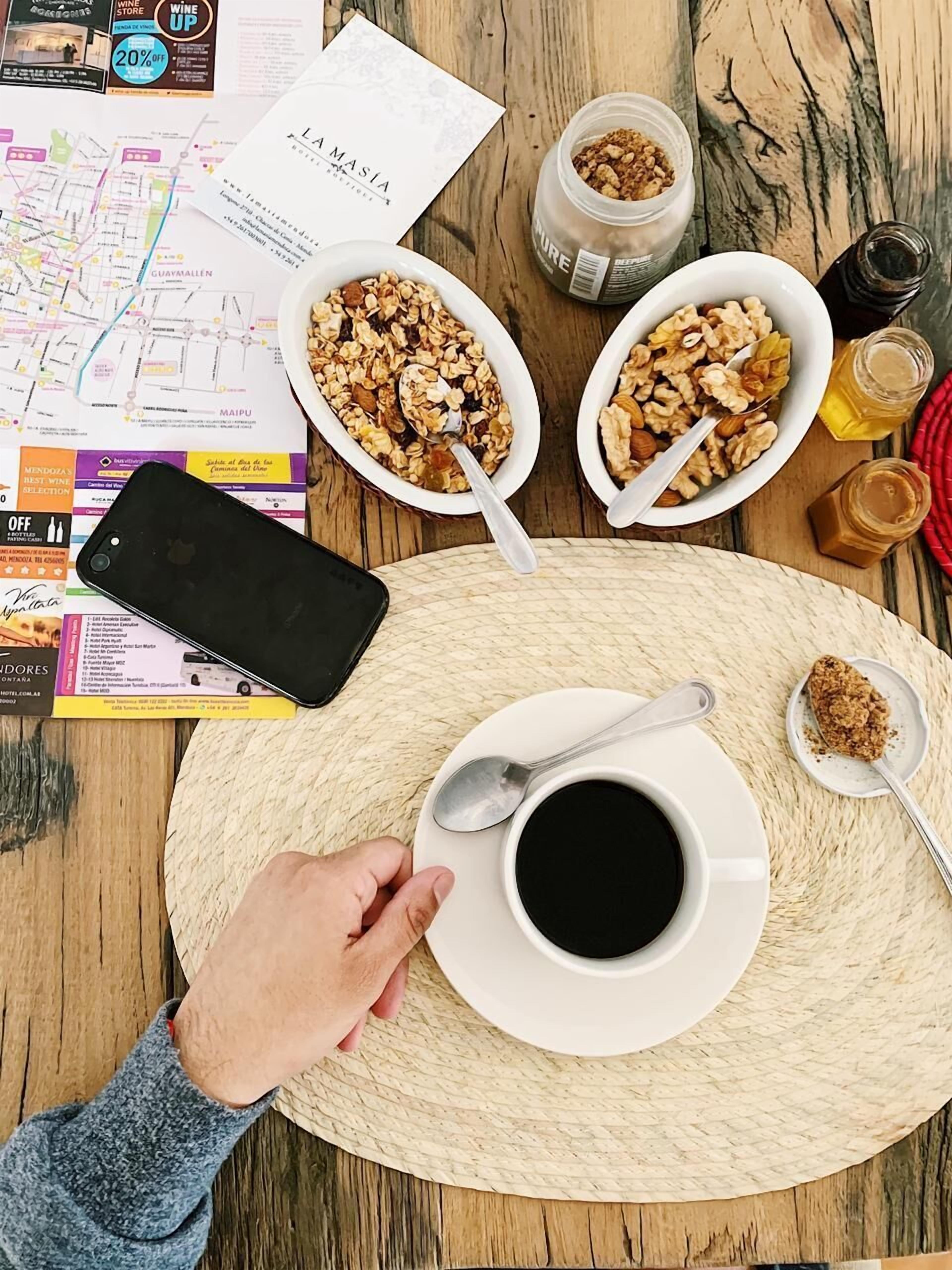 Desayuno con tazones de granola, una taza de café y un teléfono inteligente sobre un tapete tejido.