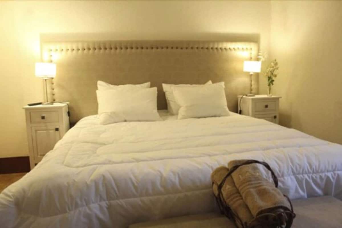 Ein ordentlich bezogenes Bett mit Kopfteil, zwei Nachttische mit Lampen und ein aufgerolltes Handtuch auf dem Bett.