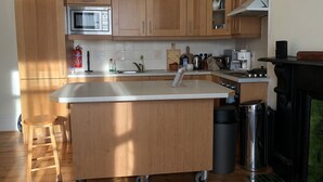 Una cocina con gabinetes de madera, un microondas de acero inoxidable, un lavamanos y una pequeña isla con un cubo de basura.