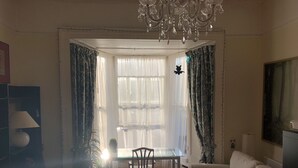 Una sala de estar con una mesa de vidrio, un sofá, una araña y un ventanal con cortinas.