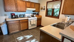 Una cocina con armarios de madera, estufa, pileta y ventana con persianas.