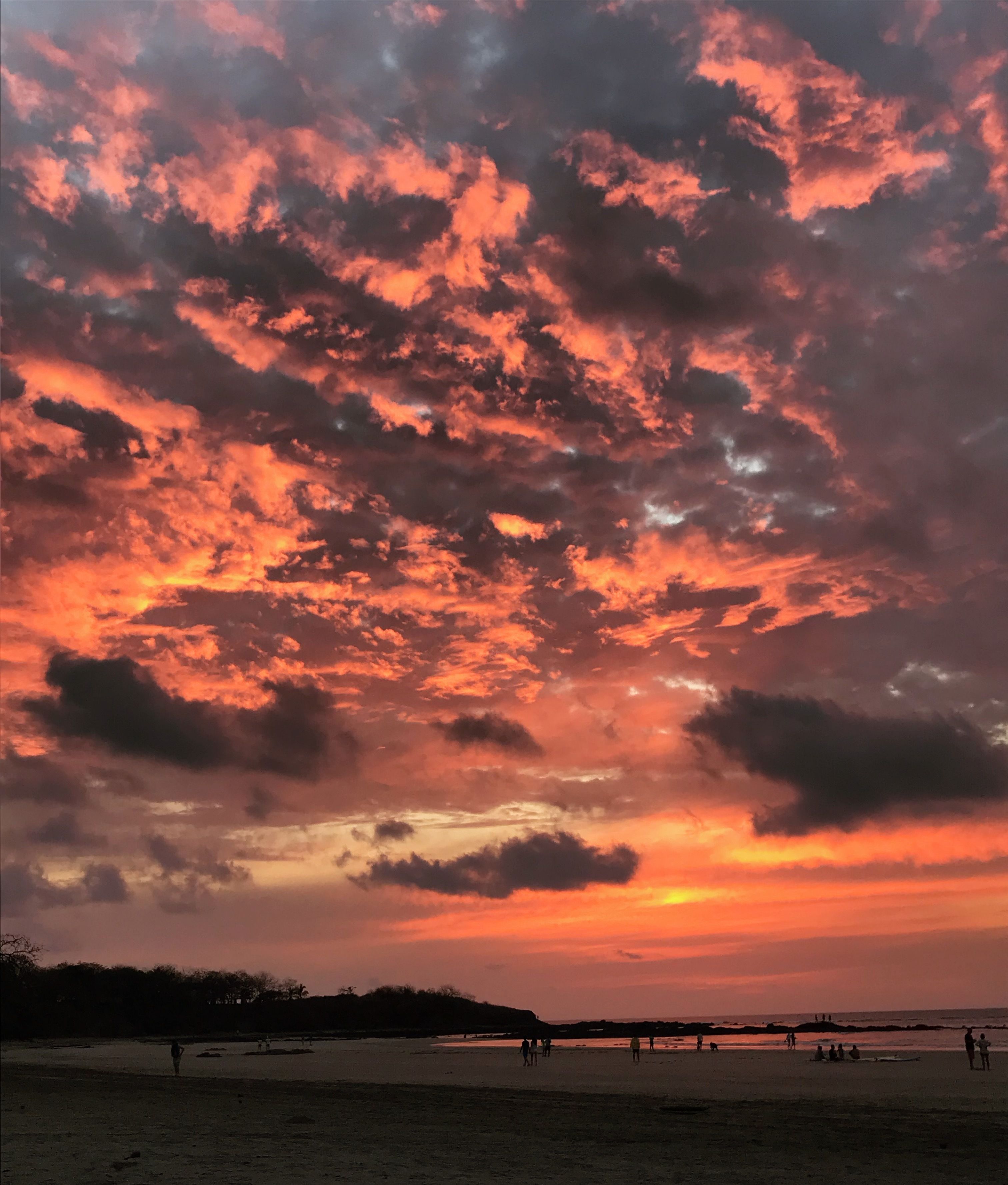 Ein Strand mit Menschen, die spazieren gehen und sitzen, und ein Sonnenuntergang mit roten Wolken.
