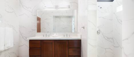 A modern bathroom with marble walls, a wooden vanity, and a skylight.