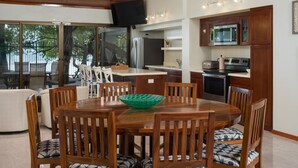 A dining area with a wooden table and chairs, a green bowl, and a kitchen with modern appliances. - Casa Woodbine Beachfront House (Tamarindo)