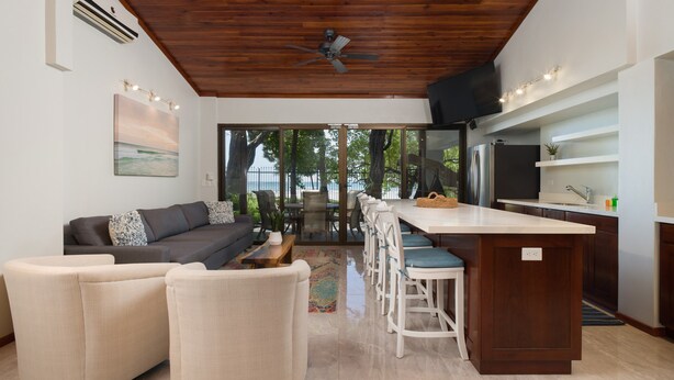 A modern kitchen with a bar area, a dining set, and a large window overlooking a garden. - Casa Woodbine Beachfront House (Tamarindo)