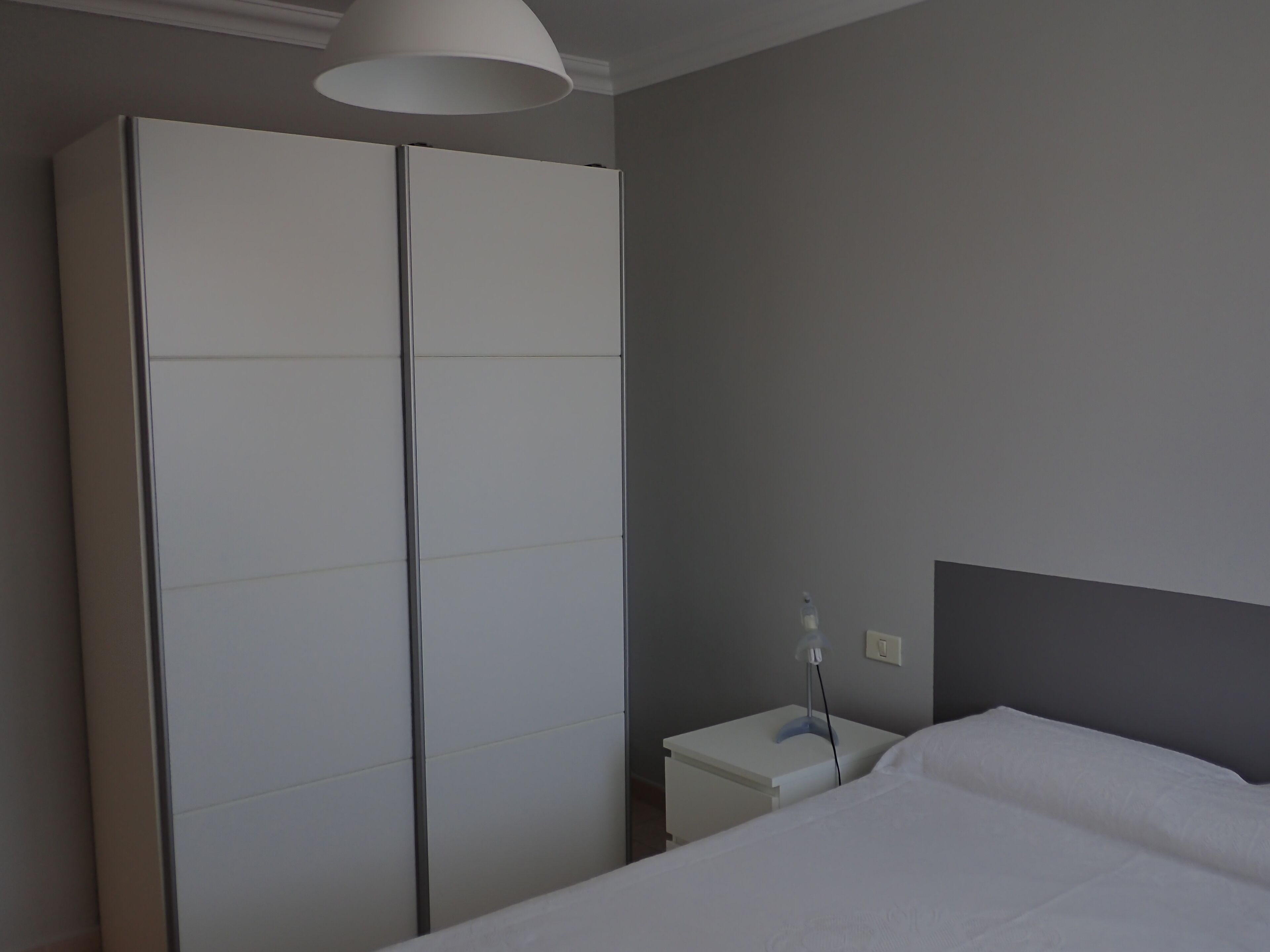 Une chambre à coucher avec un lit, une table de chevet, une armoire blanche et un luminaire au plafond.