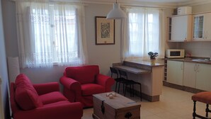 Un espacio habitable compacto con kitchenette, una zona de comedor con muebles rojos y un ventanal con cortinas translúcidas.