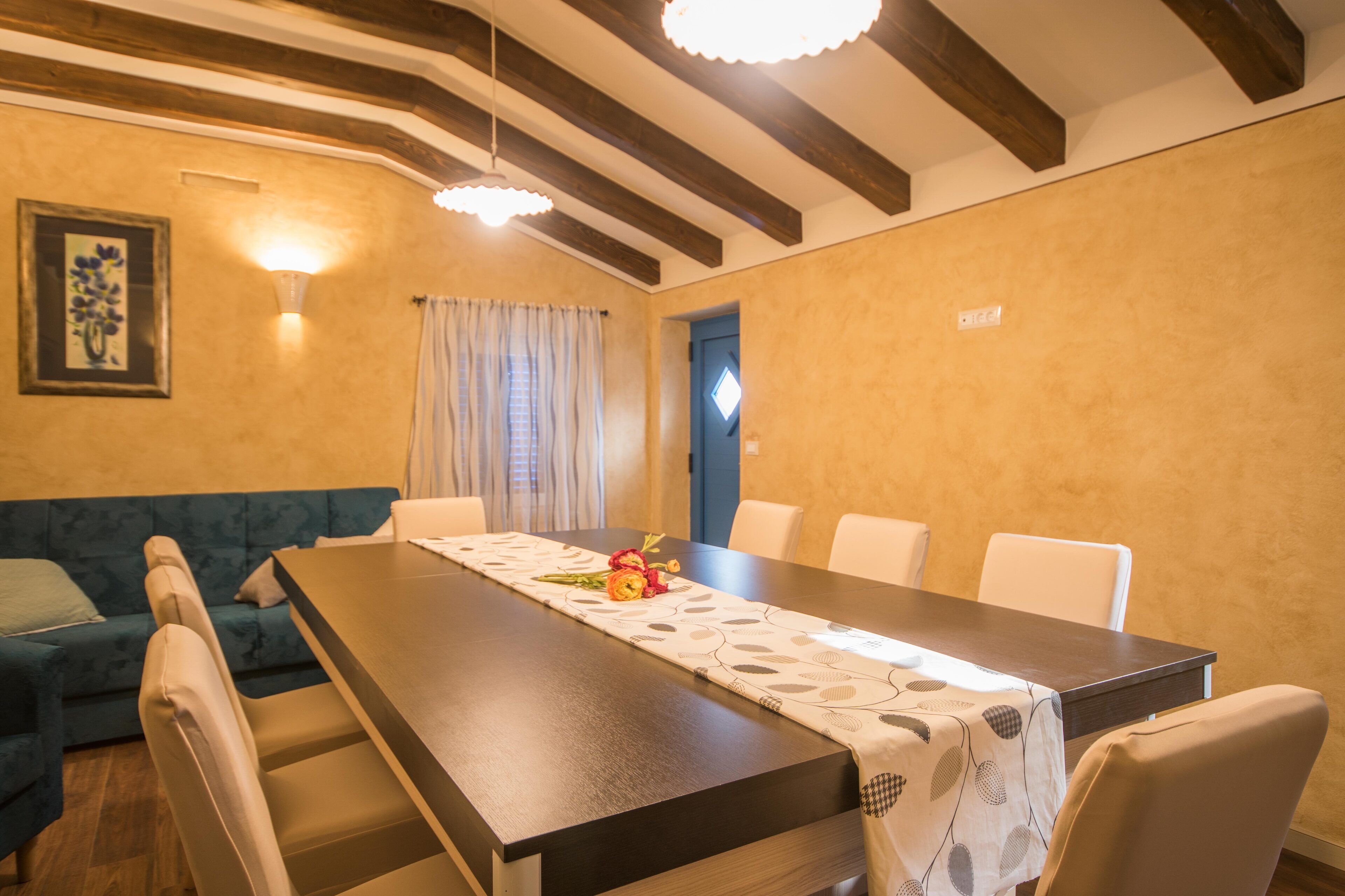 Un espace repas avec une longue table, des chaises et une composition florale en guise de centre de table.