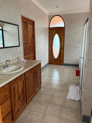 A bathroom with a sink, wooden cabinets, a mirror, and a door with a frosted glass panel.