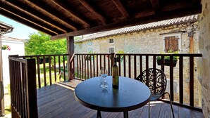 A wooden deck with a table and chairs, a bottle of wine, and a glass. A stone building with a tiled roof is visible in the background. - Traditional Stone House 3 (Buzet)