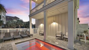 A covered outdoor swimming pool with lounge chairs and a second-floor balcony with railings. - Aria Del Mare - Beach House with Ocean Views & Private Pool Area (Miramar Beach)