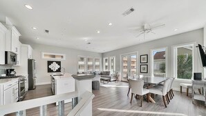 A modern kitchen with white cabinetry, a dining area with a large table and chairs, and a ceiling fan. - Aria Del Mare - Beach House with Ocean Views & Private Pool Area (Miramar Beach)