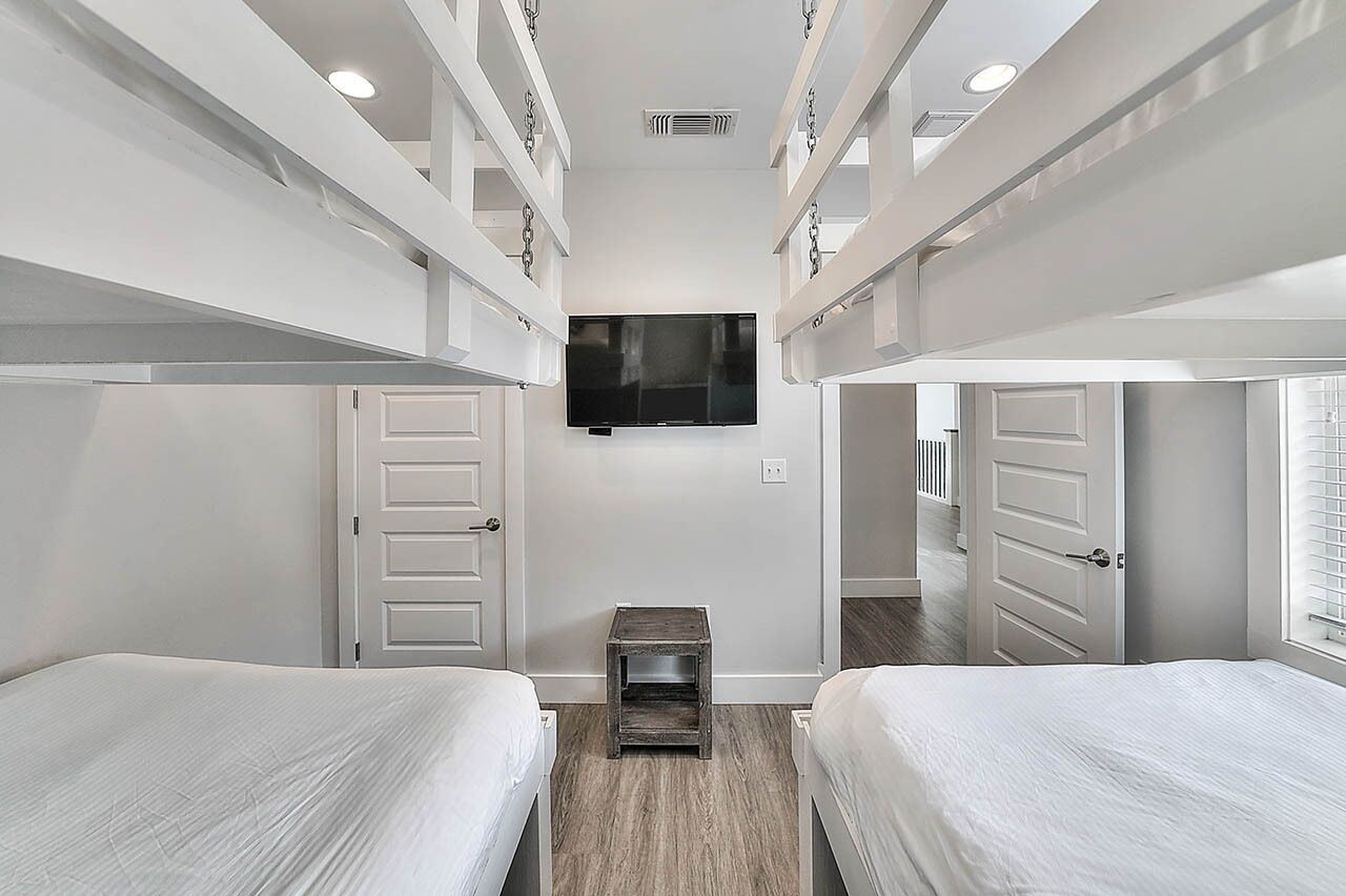 A compact, modern room with bunk beds, a small wooden nightstand, and a flat-screen TV mounted on the wall.