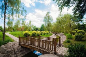 Uma ponte de madeira sobre um pequeno riacho em um jardim bem cuidado, com caminhos e vegetação.