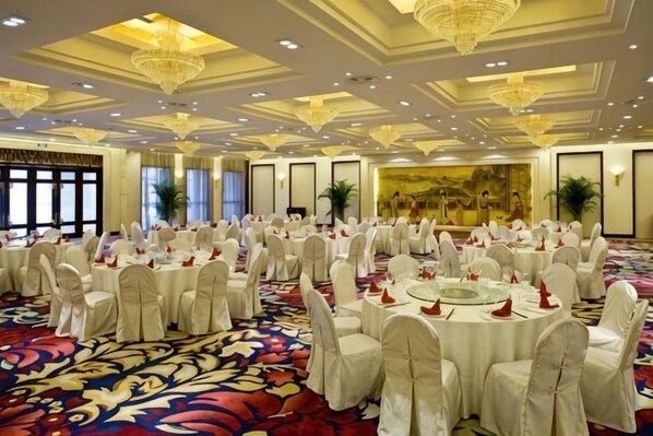 Un salón de banquetes con mesas redondas, sillas blancas y suelo alfombrado.