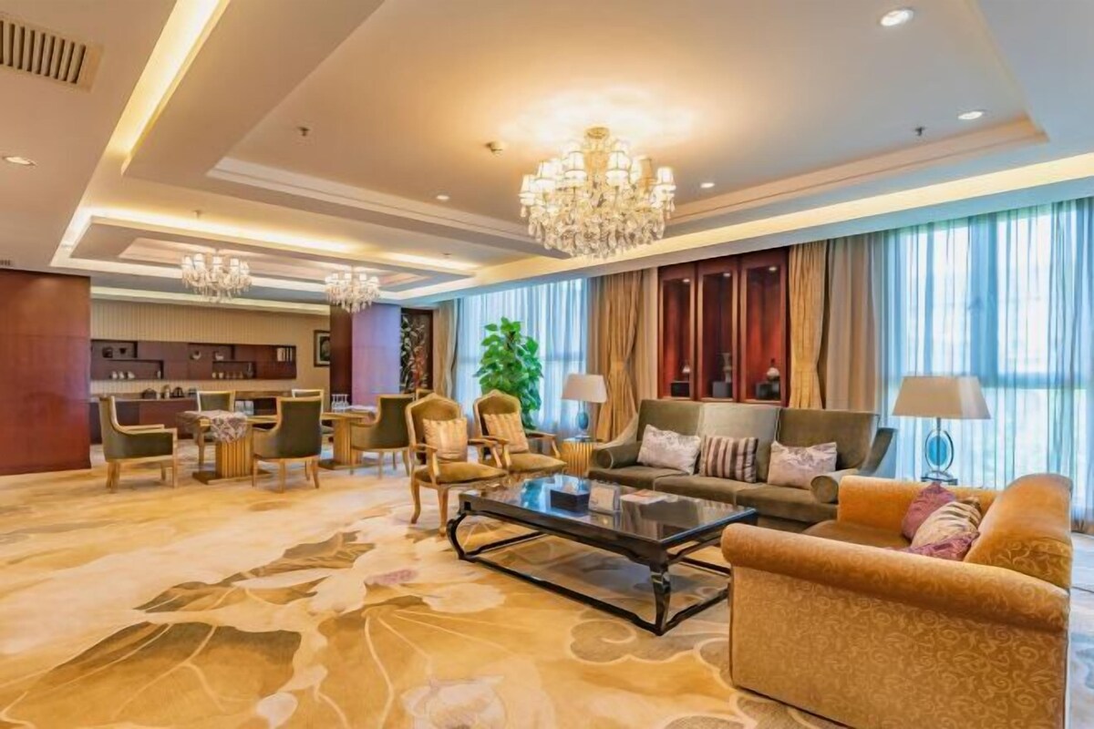 Um amplo hall de hotel com área de estar generosa, um candelabro e vista da cidade por grandes janelas.