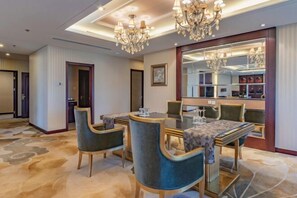 Uma sala de jantar de hotel com uma grande mesa redonda, cadeiras estofadas e um candelabro.
