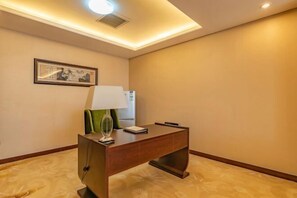 Quarto de hotel com escrivaninha de madeira, luminária, obra de arte emoldurada na parede e luz no teto.
