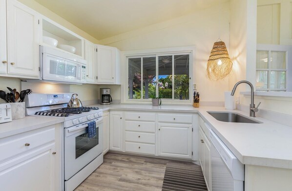A modern kitchen with white cabinetry, a gas stove, a microwave, and a coffee maker.