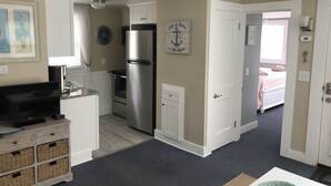 A compact kitchen with a refrigerator, oven, and a dining area with a table and chairs. - Steps to the beach with an ocean view,  (Barnstable)