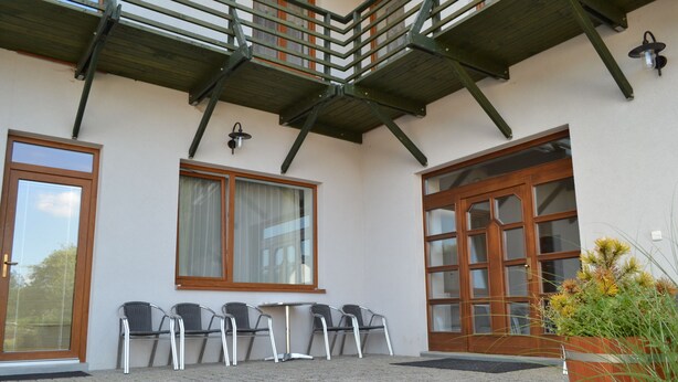 A building with a covered patio area, a wooden door, and a window with a curtain. - Farm Kundratice (Kundratice)