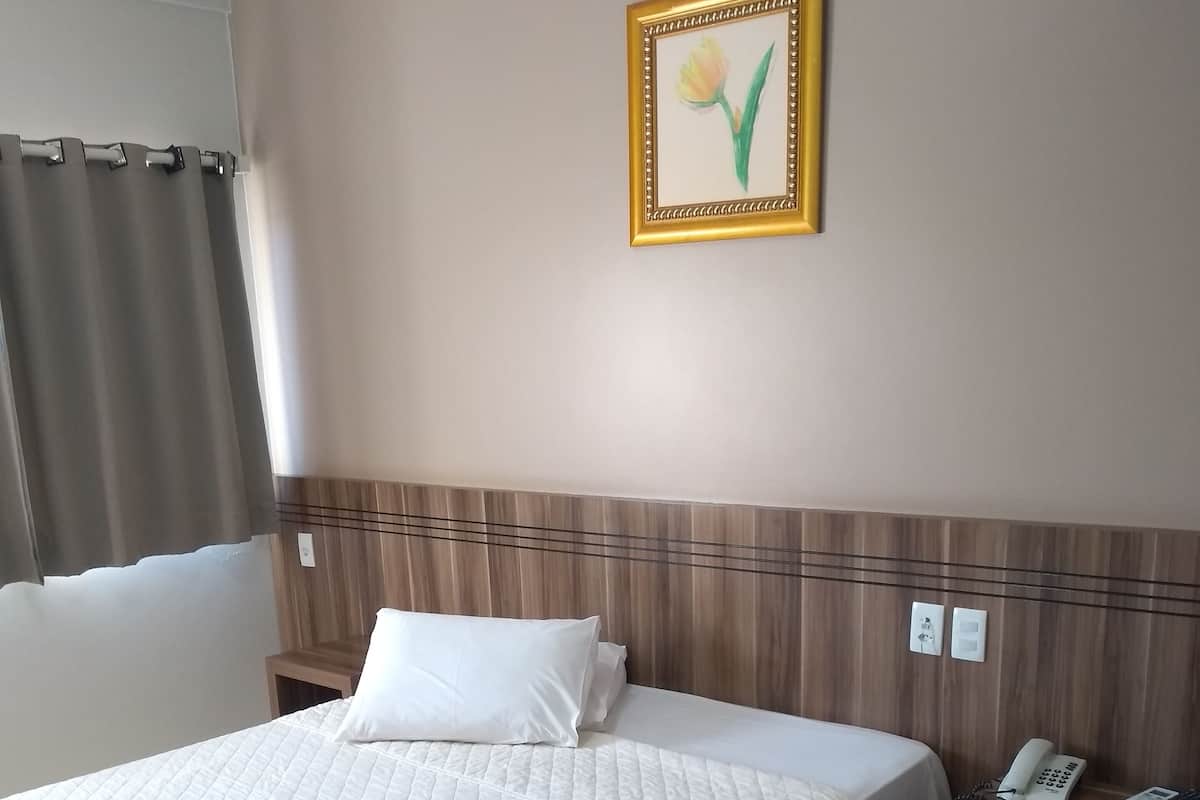 A neatly made bed with white linens and towels, a wooden nightstand with a phone and a lamp, and a framed picture of a tulip on the wall.