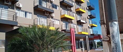 A multi-story residential building with balconies, air conditioning units, and a palm tree in the foreground.