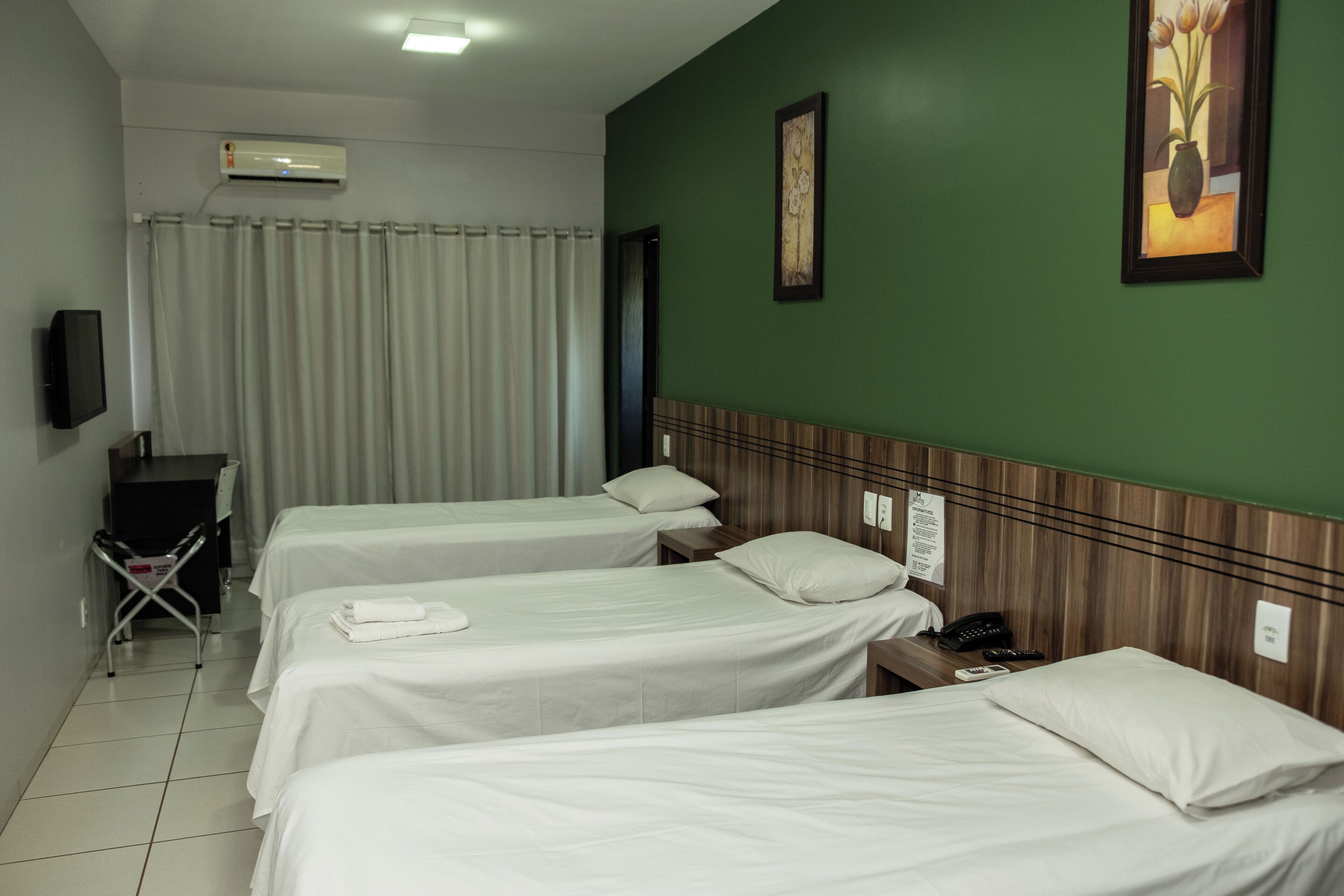 Una habitación de hotel con tres camas, un escritorio, una silla y aire acondicionado.