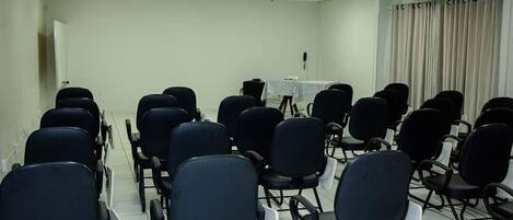 A conference room with rows of black chairs, a projector, and a table with a white tablecloth.