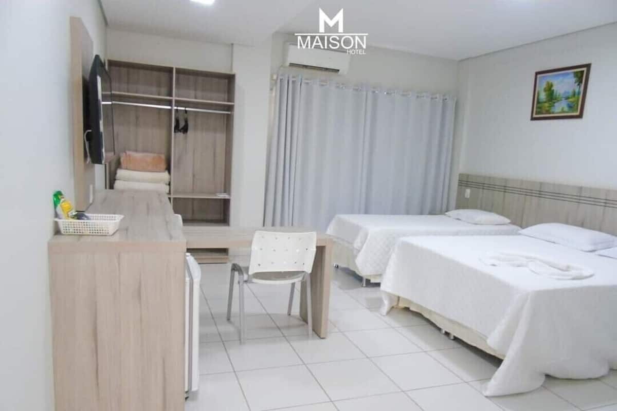 A hotel room with a desk, two beds, a chair, a wardrobe, and a window with curtains.