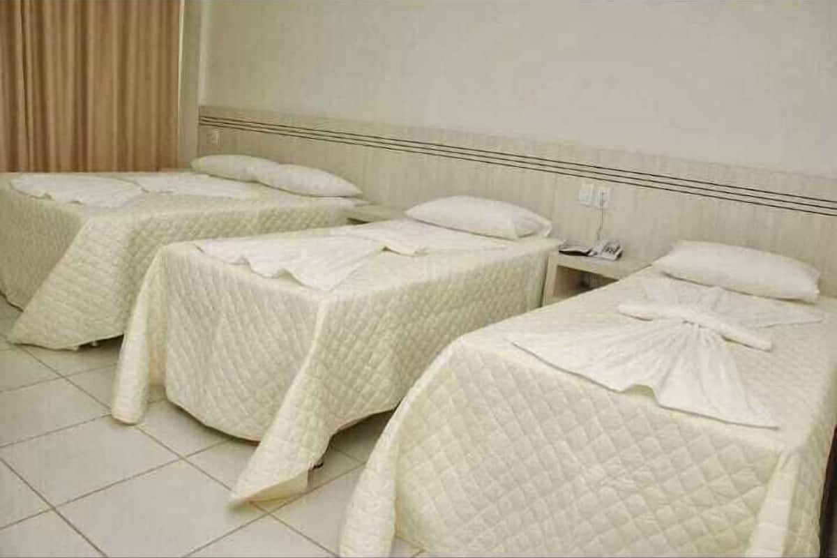 A hotel room with three single beds, each with a quilted bedspread and pillows.