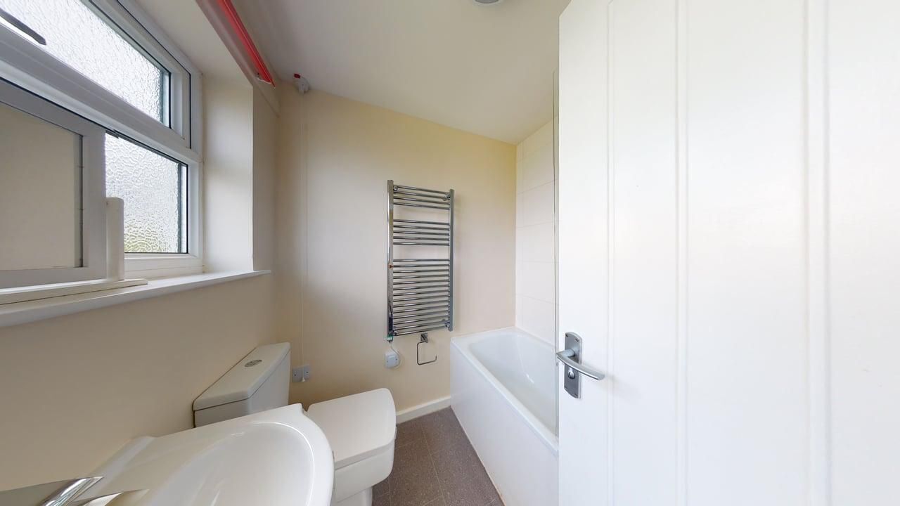 Et lille, rent badeværelse med toilet, badekar og et vindue.
