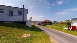 Un quartier résidentiel avec une maison blanche, une poubelle rouge et un ciel dégagé.