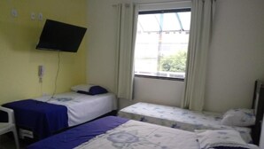 A room with two single beds, a TV mounted on the wall, and a window with curtains.