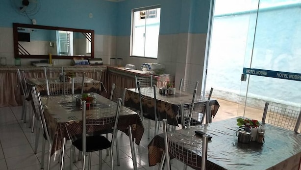 A dining area with multiple tables and chairs, a large window with a view, and a sign reading "HOTEL NOBRE".