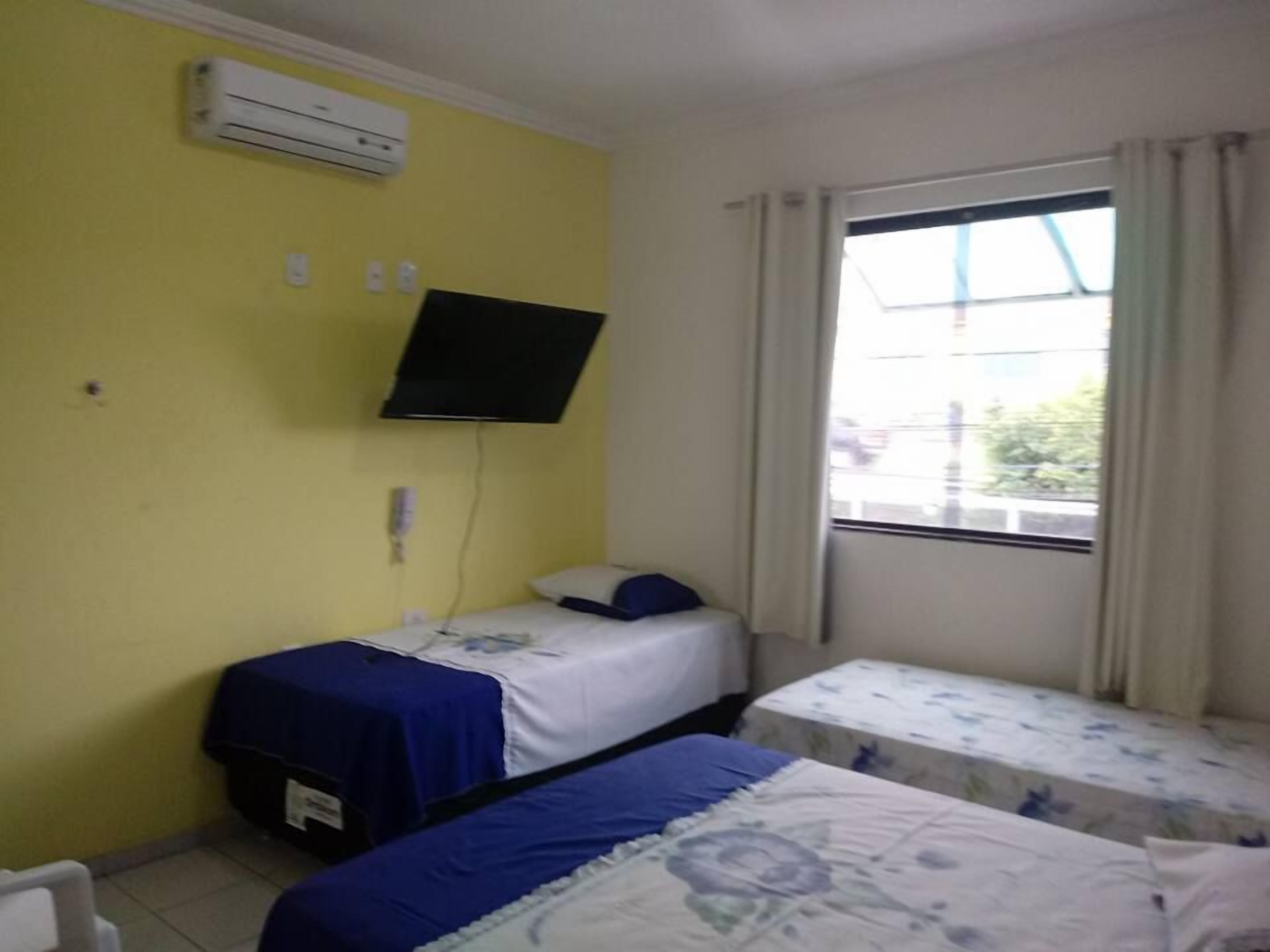 Una habitación con dos camas, aire acondicionado, televisión y ventana con cortinas.