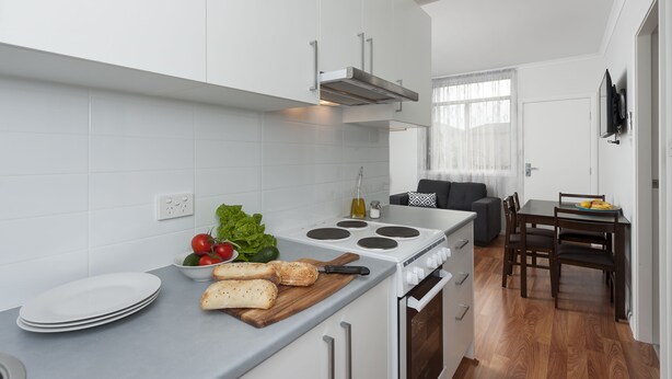 A modern kitchen with white cabinets, a stove, and a dining area with a table and chairs. - 125 Milton (Milton)