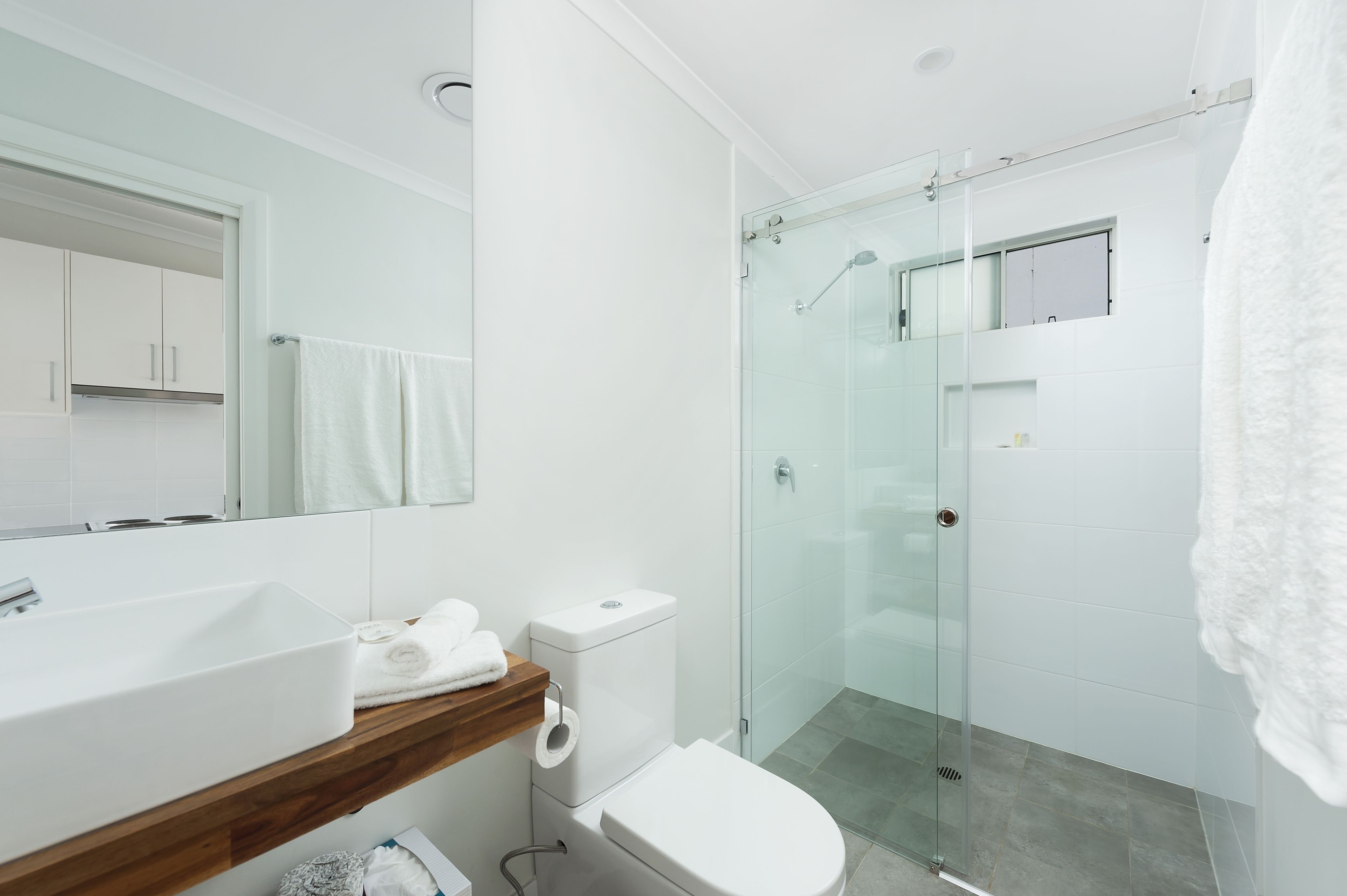 A modern bathroom with a glass-enclosed shower, a white sink, and a wooden vanity.