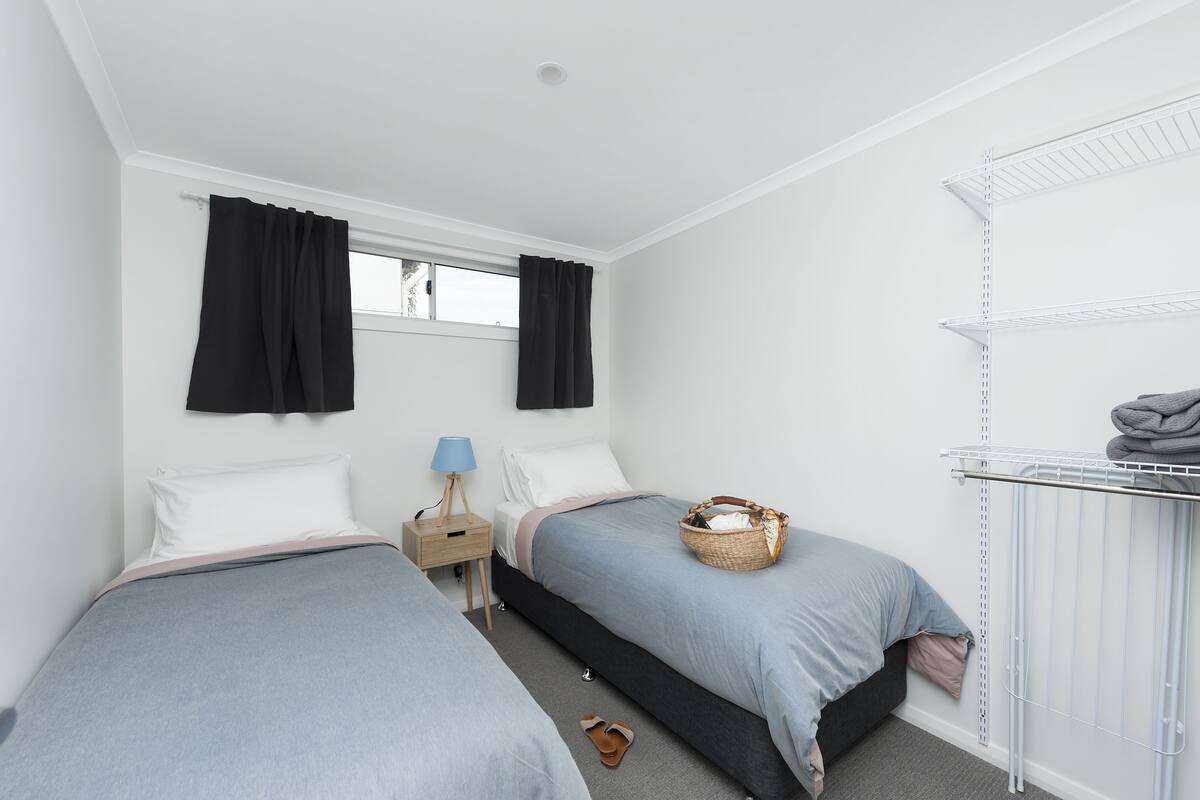 A bedroom with two beds, a nightstand, a lamp, a basket, and a radiator.