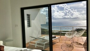 Une chambre moderne dotée d’une grande porte-fenêtre coulissante qui donne sur une terrasse extérieure offrant une vue sur la mer.
