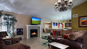 A living room with a fireplace, a television, and a dining area in the background. - Windrose McCormick Ranch (Scottsdale)