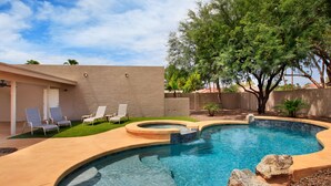 A swimming pool with a curved design, surrounded by a beige wall and a small grassy area. - Windrose McCormick Ranch (Scottsdale)