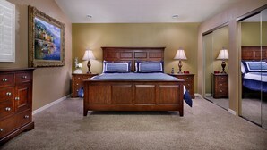 A bedroom with a large bed, wooden headboard, two bedside tables with lamps, a dresser, and a painting on the wall. - Windrose McCormick Ranch (Scottsdale)
