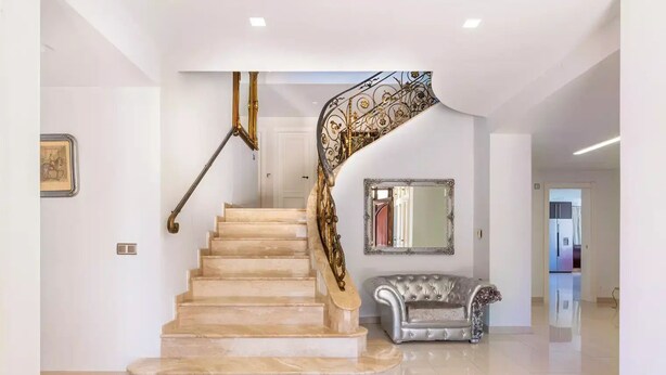 A marble staircase with ornate metal railings leading to a landing. A mirror and a tufted sofa are visible on the landing. - Ohana1 Luxury villa. (Málaga)