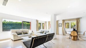 A spacious living room with a white sofa set, a black-framed sofa, a glass coffee table, and a round dining table with two chairs. - Ohana1 Luxury villa. (Málaga)