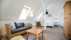 Un cuarto tipo loft con techo alto, un sofá, una silla, una mesa de madera y un armario.