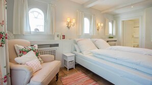 Un dormitorio con cama, mesita de noche, silla, radiador y ventana con cortinas.
