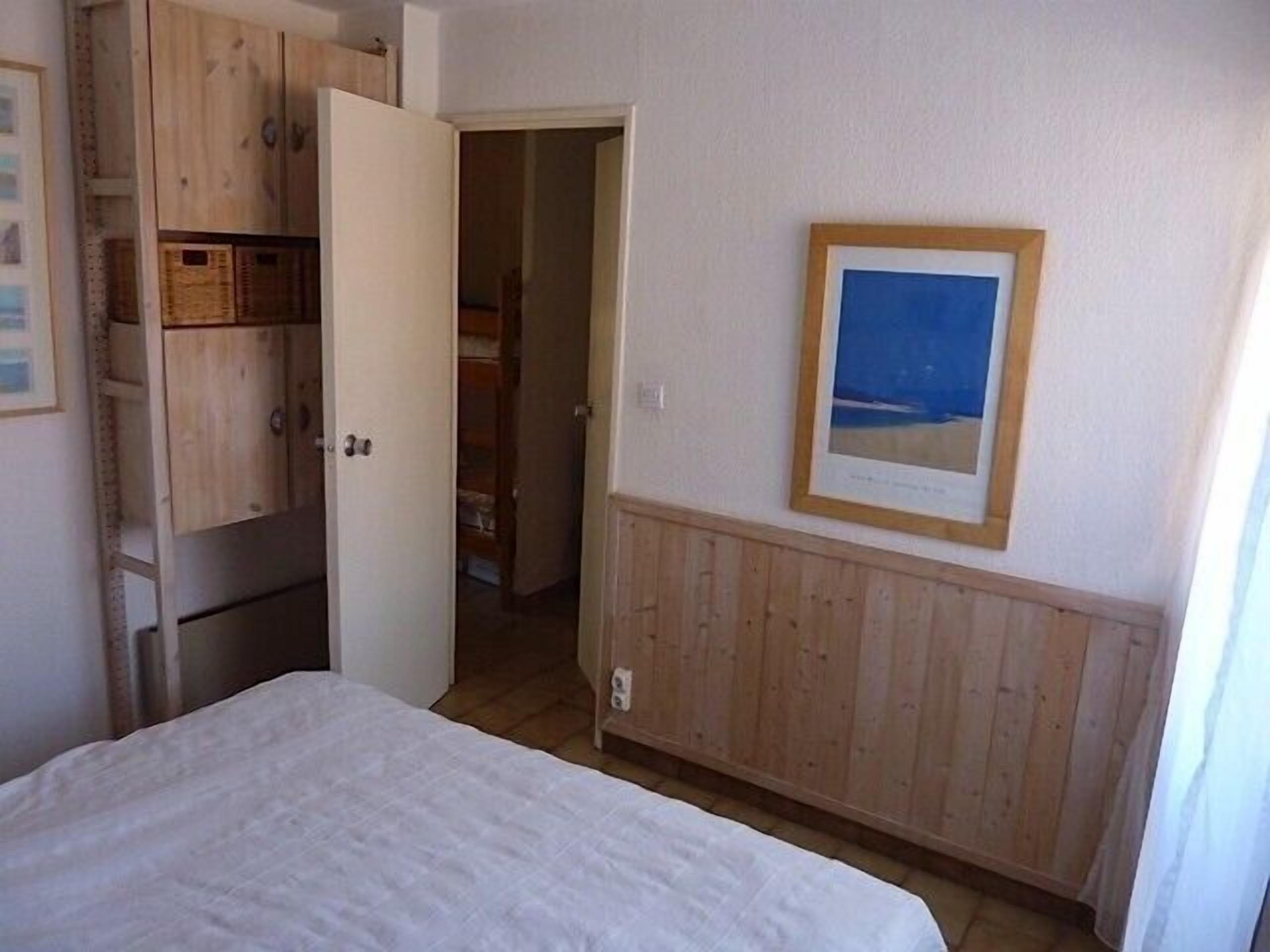 A bedroom with a bed, wooden wardrobe, and a framed picture on the wall.