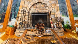 L’intérieur d’une cabane en rondins, avec une cheminée en pierre, des poutres en bois et de grandes fenêtres.